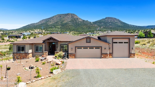 view of front facade with a garage, stone siding, a mountain view, and stucco siding