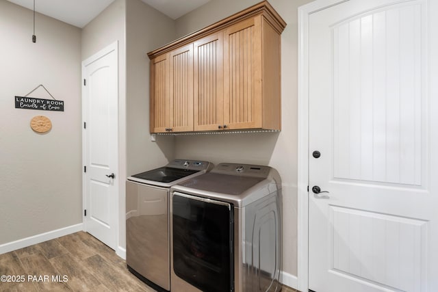 laundry room with wood finished floors, washing machine and dryer, cabinet space, and baseboards