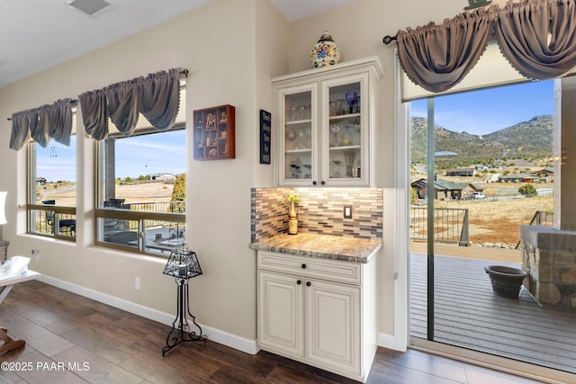 interior space featuring tasteful backsplash, visible vents, glass insert cabinets, and baseboards