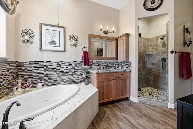 full bath with wood finished floors, vanity, a tub with jets, a stall shower, and tasteful backsplash