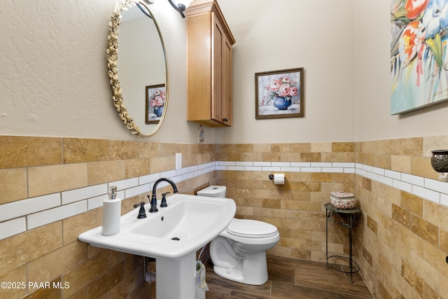 half bathroom featuring tile walls, toilet, a wainscoted wall, wood finished floors, and a sink