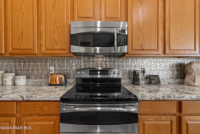 kitchen with backsplash, appliances with stainless steel finishes, and light stone countertops