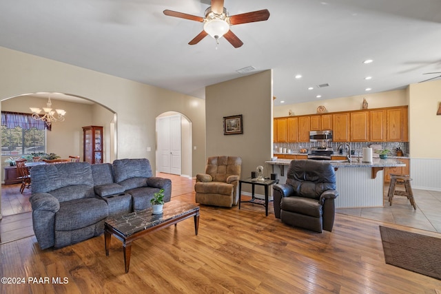 living area with visible vents, arched walkways, light wood-style flooring, and ceiling fan with notable chandelier