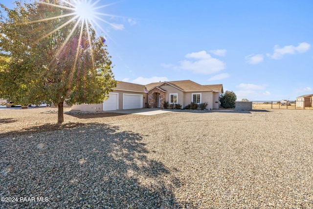single story home featuring stucco siding, driveway, stone siding, fence, and an attached garage