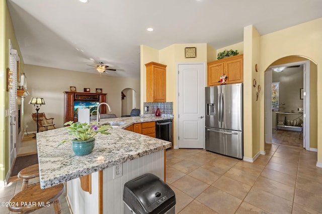 kitchen featuring ceiling fan, arched walkways, stainless steel fridge, and a sink