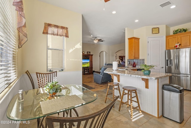 kitchen featuring a breakfast bar area, visible vents, stainless steel fridge, and ceiling fan