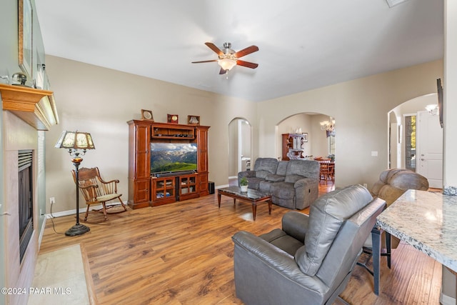 living room with a ceiling fan, arched walkways, a fireplace, light wood finished floors, and baseboards
