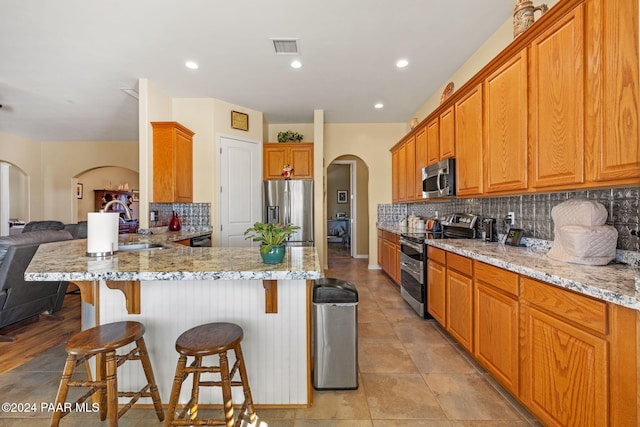 kitchen with tasteful backsplash, light stone countertops, arched walkways, and stainless steel appliances