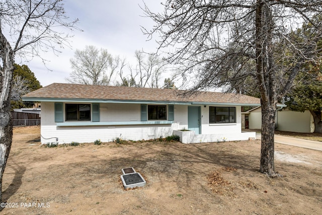 ranch-style home featuring a shingled roof and fence