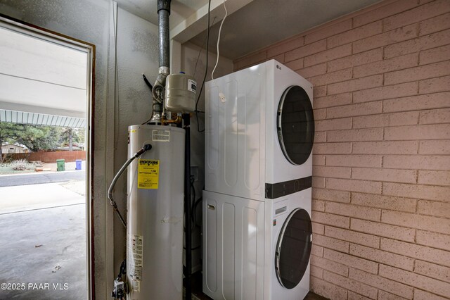 clothes washing area with stacked washer / dryer, laundry area, water heater, and brick wall