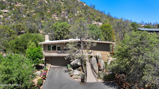 2009 Rocky Dells Dr, Prescott, AZ 86303 - view of front of home with an attached garage, asphalt driveway, a chimney, a balcony, and a wooded view