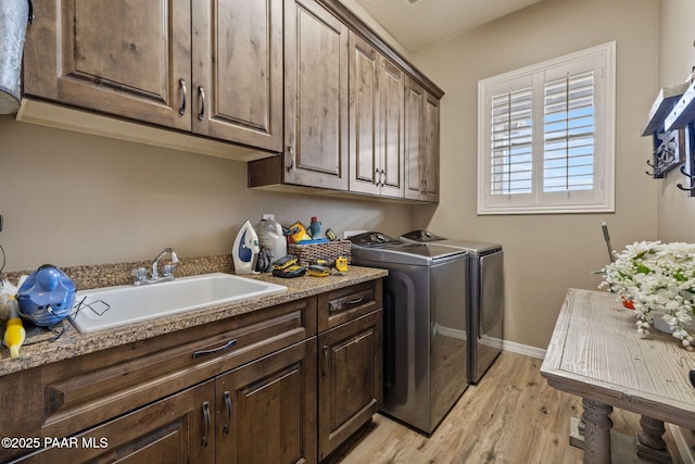 clothes washing area with washing machine and clothes dryer, cabinet space, light wood finished floors, and baseboards