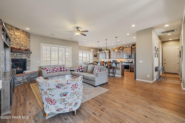 living area with a ceiling fan, a stone fireplace, light wood-style floors, recessed lighting, and baseboards