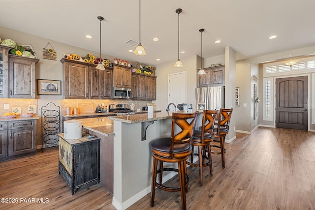 kitchen with appliances with stainless steel finishes, light wood-style floors, an island with sink, decorative backsplash, and light stone counters