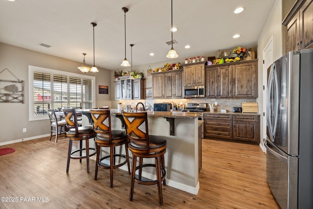 kitchen with stainless steel appliances, a kitchen bar, a center island with sink, light wood-style flooring, and tasteful backsplash