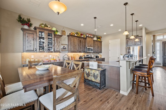 kitchen featuring stainless steel appliances, wood finished floors, decorative backsplash, a spacious island, and hanging light fixtures