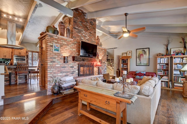 living room with vaulted ceiling with beams, a brick fireplace, ceiling fan, and dark wood-style flooring
