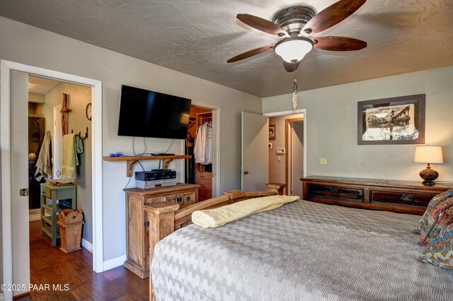 bedroom featuring dark wood-style flooring, a spacious closet, ceiling fan, a textured ceiling, and baseboards