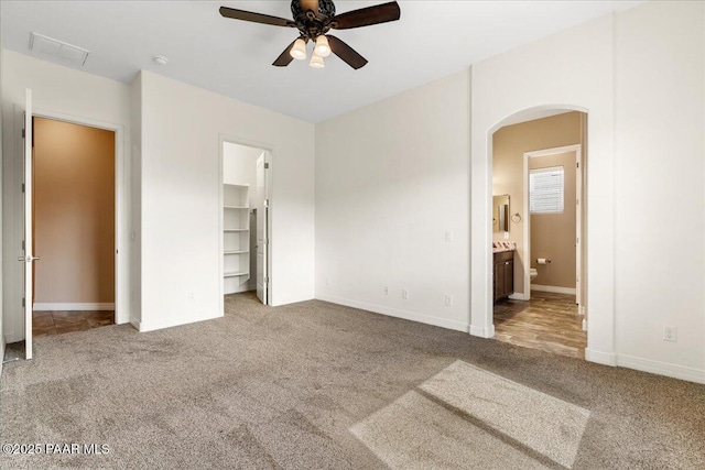 unfurnished bedroom with a walk in closet, carpet floors, arched walkways, and ensuite bath