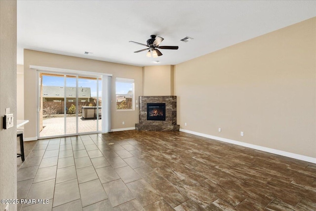 unfurnished living room featuring baseboards, visible vents, a stone fireplace, and ceiling fan