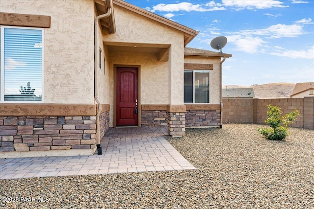 view of exterior entry featuring stucco siding, stone siding, and fence