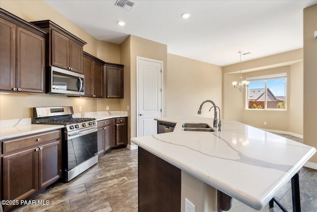 kitchen featuring visible vents, a kitchen island with sink, a sink, light stone counters, and appliances with stainless steel finishes