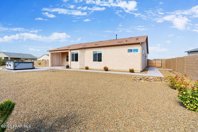 rear view of house with a patio area, stucco siding, a hot tub, and a fenced backyard