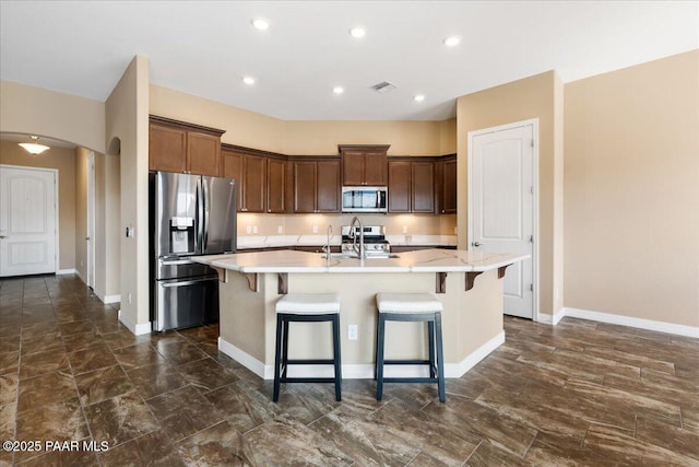 kitchen with stainless steel appliances, arched walkways, a center island with sink, and light countertops