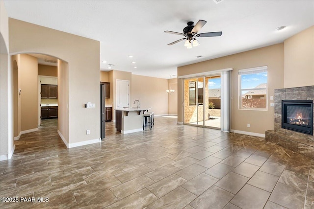 unfurnished living room with ceiling fan with notable chandelier, recessed lighting, arched walkways, baseboards, and a tile fireplace