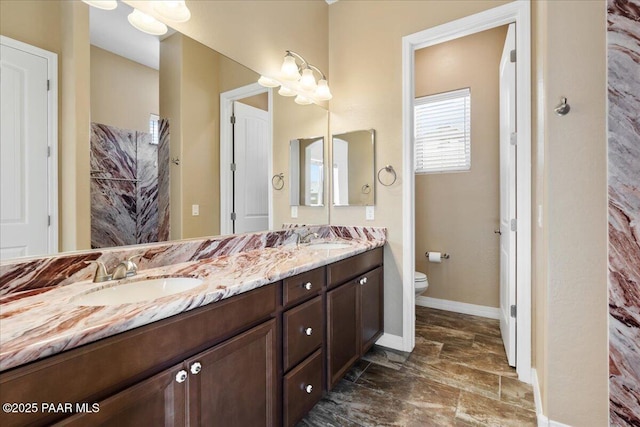 full bath with a sink, baseboards, toilet, and double vanity