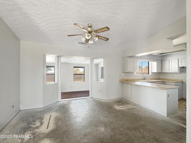 kitchen featuring visible vents, a ceiling fan, a sink, concrete floors, and a peninsula