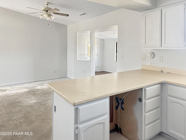 kitchen with light countertops, a peninsula, white cabinets, a textured ceiling, and a ceiling fan