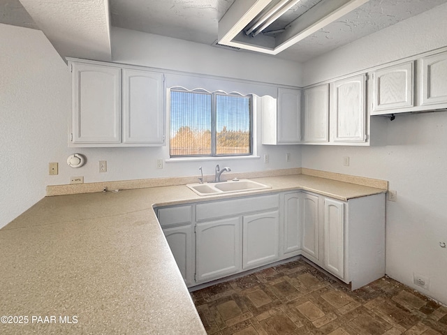 kitchen with a sink, light countertops, dark floors, and white cabinetry