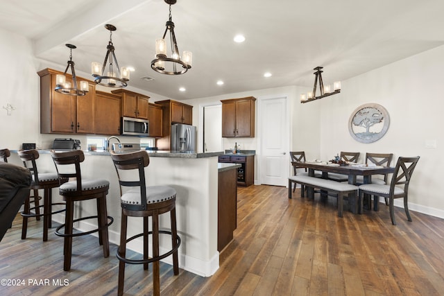 kitchen featuring a breakfast bar, appliances with stainless steel finishes, decorative light fixtures, and dark wood-type flooring