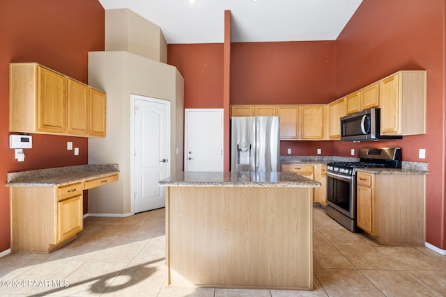 kitchen with light brown cabinetry, a kitchen island, stainless steel appliances, and light tile patterned floors