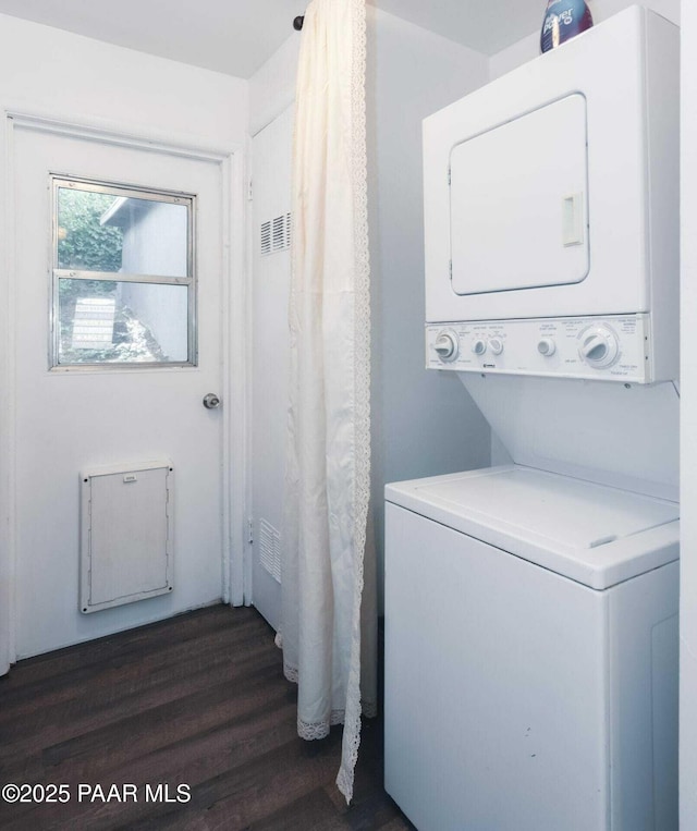 clothes washing area with laundry area, stacked washer and clothes dryer, dark wood-type flooring, and visible vents