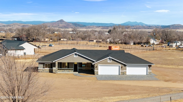 view of front of property featuring stone siding, dirt driveway, a mountain view, fence, and a garage