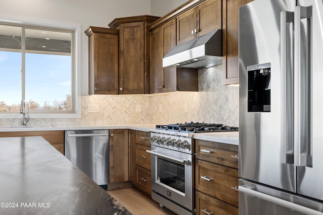 kitchen with decorative backsplash, stainless steel appliances, under cabinet range hood, and a sink