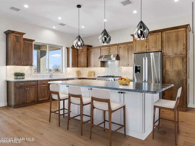 kitchen with a kitchen island, under cabinet range hood, visible vents, and stainless steel fridge