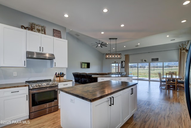kitchen with butcher block counters, electric range, under cabinet range hood, open floor plan, and a center island