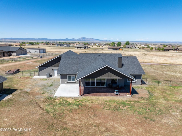 view of front of house featuring a patio area, roof with shingles, a fenced backyard, and a mountain view