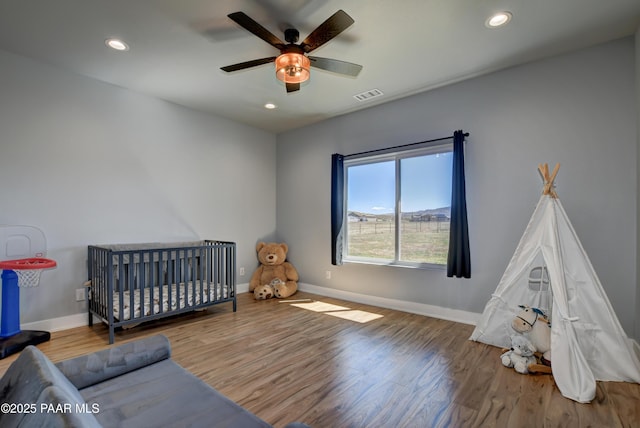 bedroom featuring wood finished floors, baseboards, recessed lighting, ceiling fan, and a nursery area