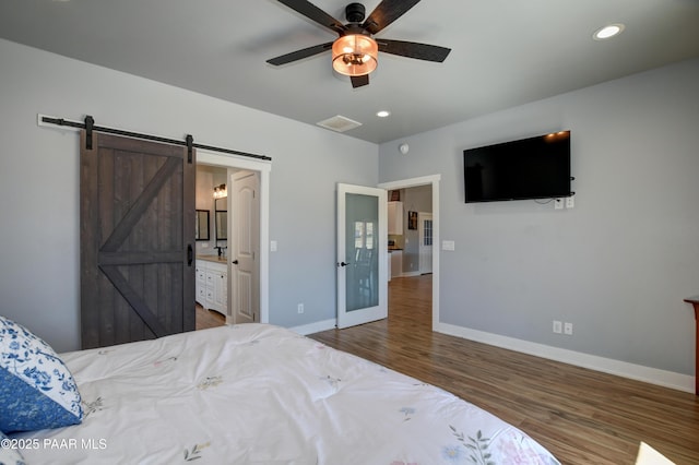bedroom with a barn door, baseboards, wood finished floors, recessed lighting, and connected bathroom