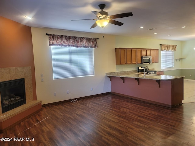 kitchen featuring ceiling fan, dark hardwood / wood-style flooring, a tiled fireplace, a breakfast bar, and appliances with stainless steel finishes