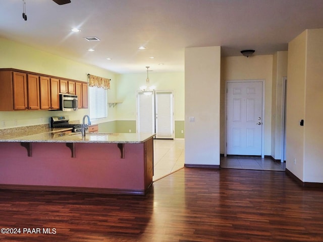 kitchen featuring a breakfast bar, dark hardwood / wood-style floors, decorative light fixtures, light stone counters, and stainless steel appliances