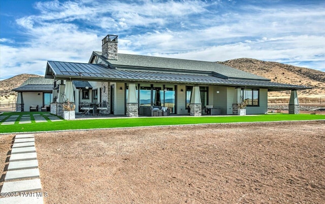 back of property with a standing seam roof, a mountain view, a chimney, and metal roof