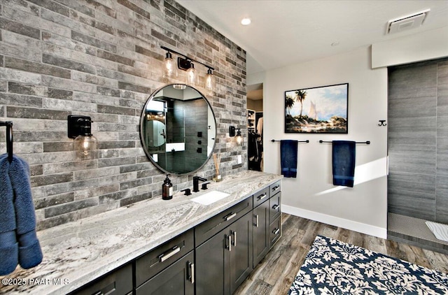 full bath with visible vents, wood finished floors, baseboards, vanity, and tiled shower