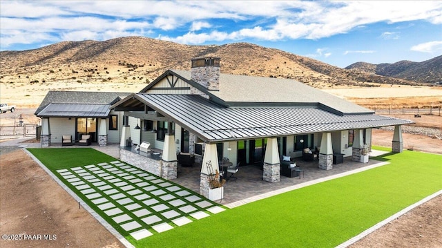 rear view of property with a patio, a standing seam roof, a mountain view, and an outdoor living space