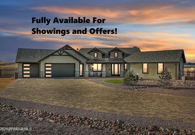 modern inspired farmhouse with a garage, fence, decorative driveway, and stone siding