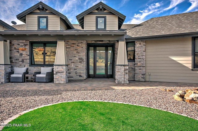 entrance to property featuring a patio, roof with shingles, and stone siding
